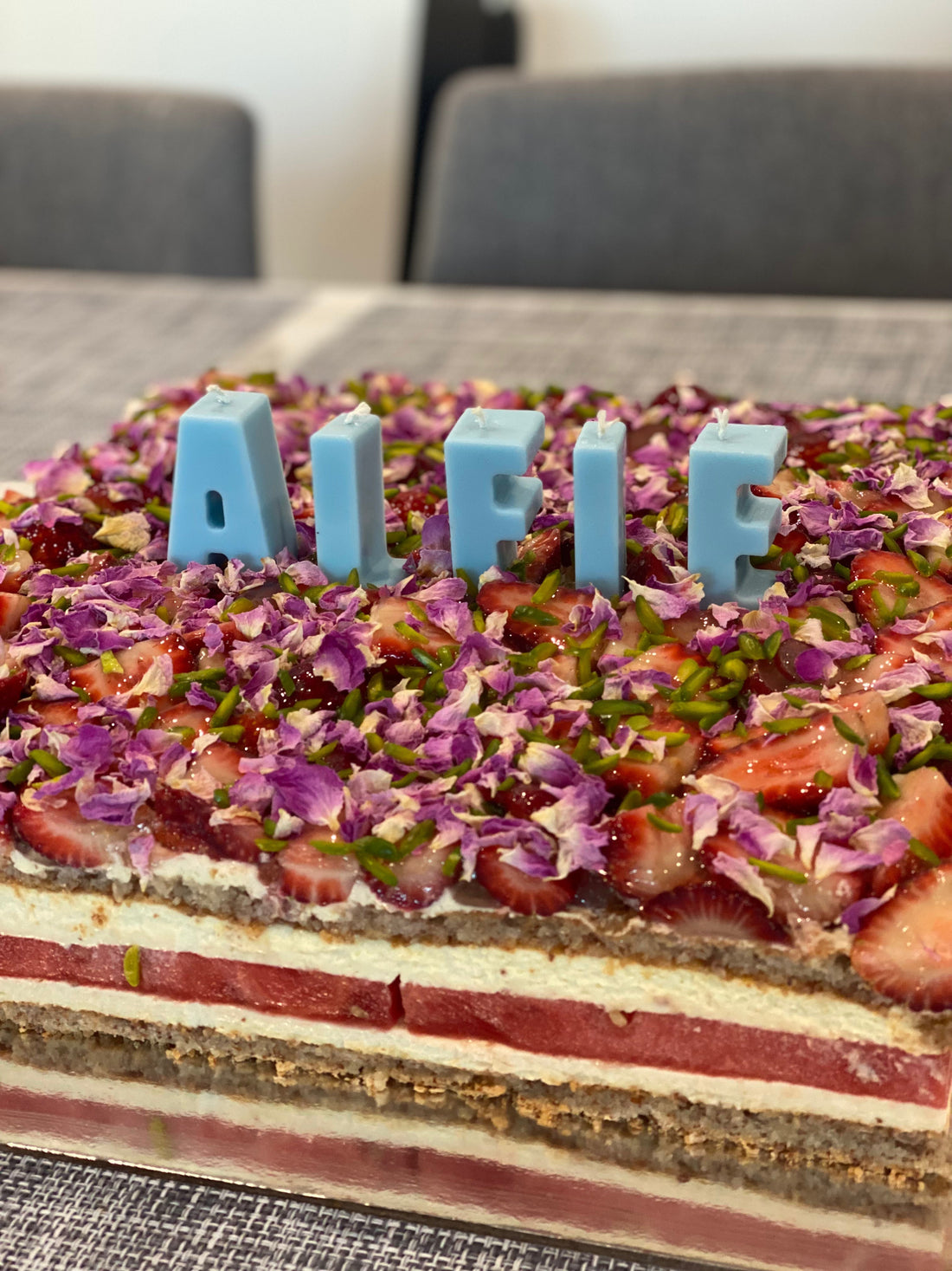 Birthday cake styled with blue birthday letter candles spelling ALFIE on a watermelon cake.