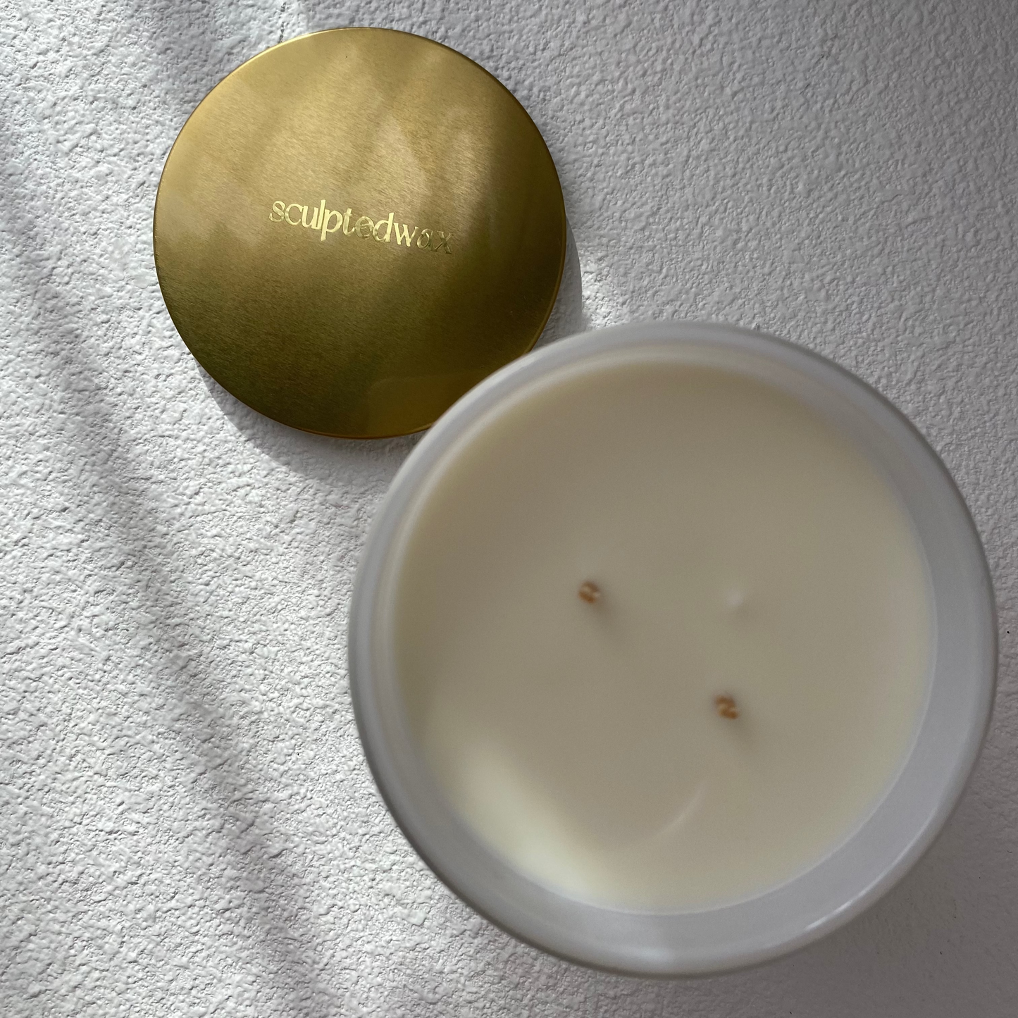 White candle and golden lid on a textured surface